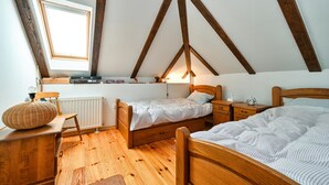 Une chambre mansardée chaleureuse avec des poutres apparentes, deux lits simples, un bureau et une fenêtre.