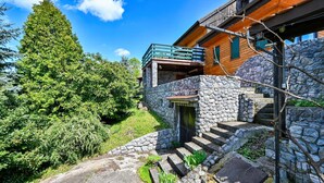 Une maison en pierre avec un balcon en bois, un escalier en pierre et un grand arbre en arrière-plan.
