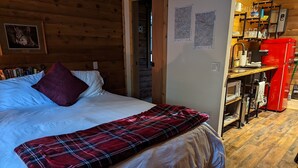 A cozy bedroom with a bed, a red plaid blanket, a wooden headboard, and a red appliance in the corner. - Studio Cabin, minutes from lake and trails (North Bend)
