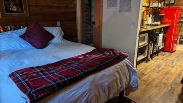 A cozy bedroom with a bed, a red plaid blanket, a wooden headboard, and a red appliance in the corner.