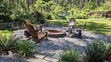 A garden area with Adirondack chairs, a fire pit, and a hammock.