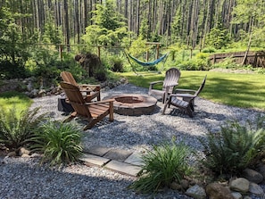 Un jardín con sillas Adirondack, una fogata y una hamaca.