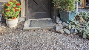 A black door with a diamond-patterned window, a potted red flowering plant, and a bamboo plant. - Studio Cabin, minutes from lake and trails (North Bend)