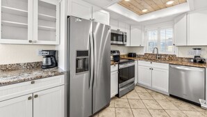 Une cuisine moderne avec des meubles blancs, des appareils en acier inoxydable, un plan de travail en granit et un plafond en bois.