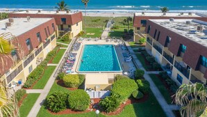 Une piscine sur le toit offrant une vue sur la plage, entourée d’immeubles dotés de balcons et d’un palmier.