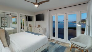 Quarto com uma cama grande, ventoinha no teto, televisão e vista para o mar pelas portas de correr.