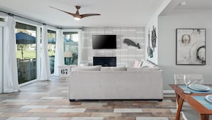 Uma sala de estar moderna com um sofá grande, uma televisão de tela plana, uma lareira e um espaço de jantar com mesa e cadeiras.