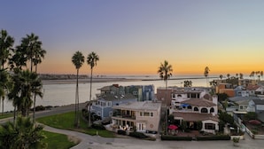 Área residencial costeira com casas, palmeiras e vista para o oceano ao pôr do sol.