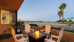 Um pátio com uma mesa quadrada e quatro cadeiras brancas, lareira e vista para a praia e palmeiras.