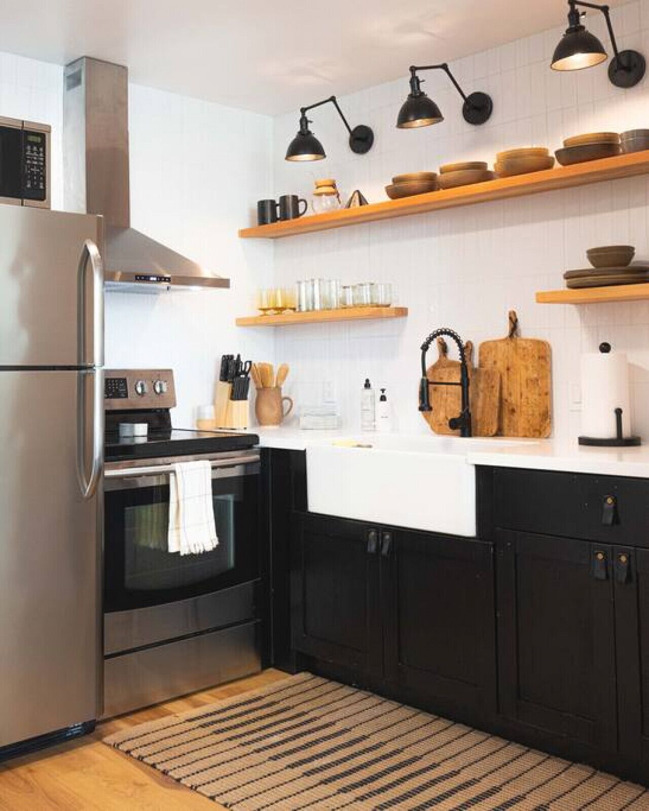 A modern kitchen with a stainless steel refrigerator, a built-in oven, black cabinets, and wooden shelves above the counter.