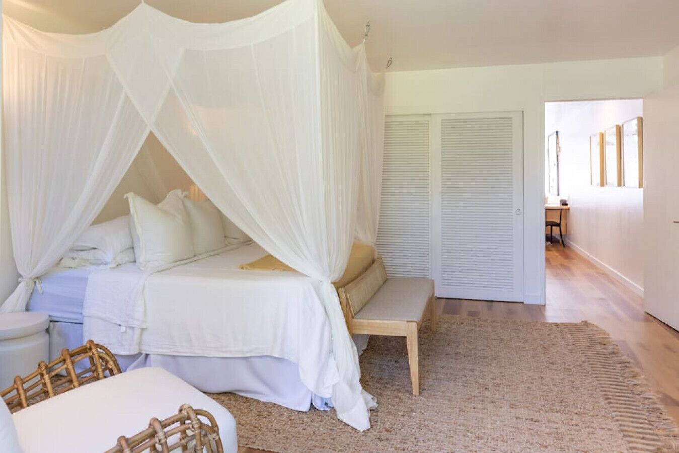 Un dormitorio con cama a dosel, un banco junto a la cama y vista a un pasillo con una puerta.