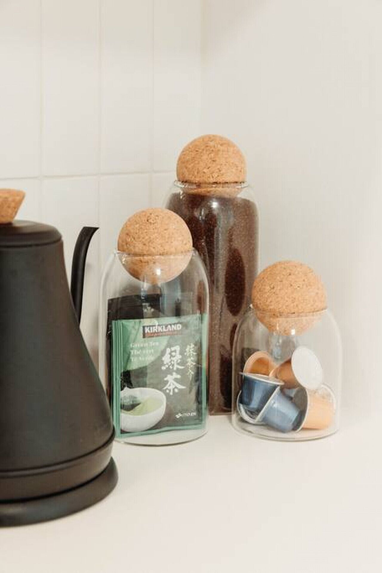 Three glass jars with cork lids, one containing a green bottle, and a black appliance in the background.