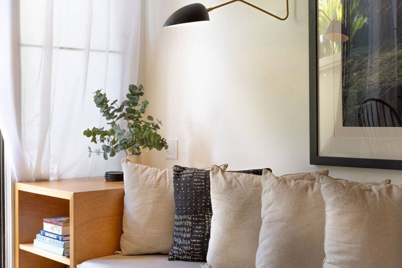 Una sala de estar moderna con una mesita de madera, una estantería, una planta en maceta y un cuadro en la pared.