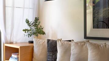 Una sala de estar moderna con una mesita de madera, una estantería, una planta en maceta y un cuadro en la pared.