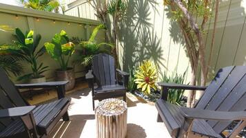 Une terrasse avec des chaises noires et une table en bois, entourée de plantes en pot et d’un petit arbre.