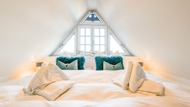 A bedroom with a sloped ceiling, a skylight, and a bed with two fluffy pillows and two towels.