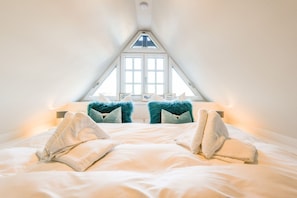 A bedroom with a sloped ceiling, a skylight, and a bed with two fluffy pillows and two towels.