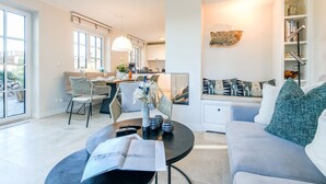A modern living room with a sofa, a dining area with chairs, and a kitchen in the background.