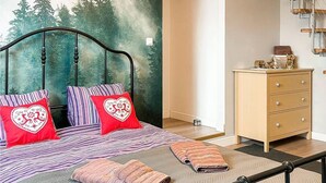 A bedroom with a bed, two pillows, a dresser, and a wall with a forest mural.
