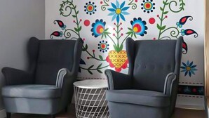 A room with two grey armchairs, a small round table, and a decorative wall mural with floral and geometric patterns.