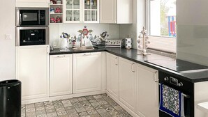 A kitchen with white cabinets, a black microwave, and a window with blinds.