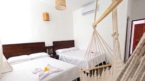 A hotel room with two beds, a macramé hanging chair, a woven light fixture, and an air conditioning unit. - Casa Ramona (Flores)