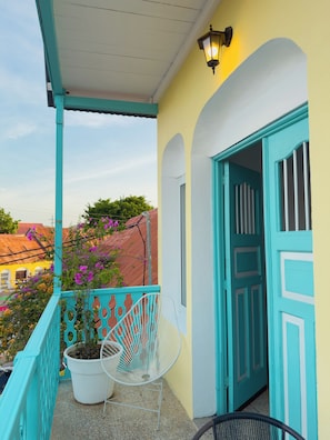 A balcony with turquoise railings, a white chair, and a potted plant.
