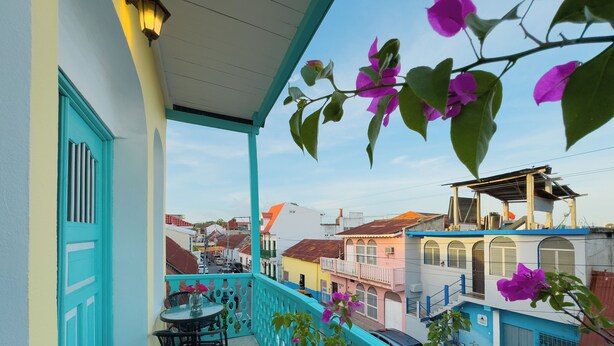 A balcony with turquoise railings, a table, and chairs, overlooking a street with colorful buildings. - Casa Ramona (Flores)