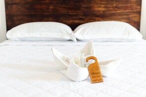A neatly made bed with a white quilt, two white pillows, and a wooden tag with the text 'Please Do not disturb' on a hotel room.