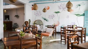 A dining area with wooden tables and chairs, hanging wicker lamps, and a wall mural of lotus flowers. - Casa Ramona (Flores)