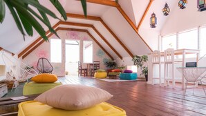 A spacious attic room with wooden beams, colorful bean bags, and a large window. - Casa Ramona (Flores)