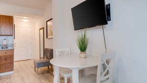A dining area with a white table and chairs, a potted plant, and a mounted flat-screen TV.