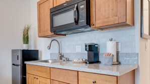A modern kitchen with wooden cabinets, a stainless steel refrigerator, a microwave, a coffee maker, and a sink.