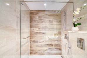 Ein modernes Badezimmer mit Duschkabine aus Glas, einer Wand mit Holzstruktur und einer weißen Orchidee in einer Vase.