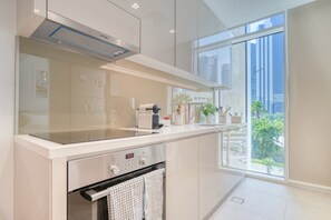 A modern kitchen with a built-in oven, a coffee maker, and a view of the city through large windows.
