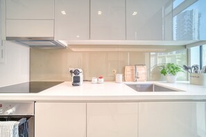 A modern kitchen with a stainless steel range hood, a built-in oven, a sink, and a window with a view of the outside. - Bright & Homey Studio Apartment in JLT (Dubai)