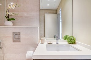 A modern bathroom with a large sink, a mirror, a potted orchid, and a small green plant. - Bright & Homey Studio Apartment in JLT (Dubai)
