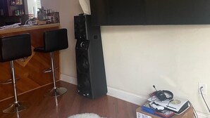 Uma sala de estar com uma grande TV de tela plana na parede, um tapete felpudo branco e dois banquetas pretas.