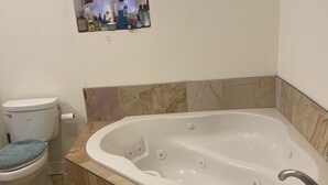 Casa de banho com banheira, sanita e uma pequena janela com cortina.