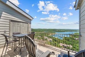 A balcony with a table and chairs, overlooking a lake with boats and a forested landscape. - Private Deck, Bunk Bed, Games & Stunning Lake Views, Near Silver Dollar City with Free Daily Fun (Branson)