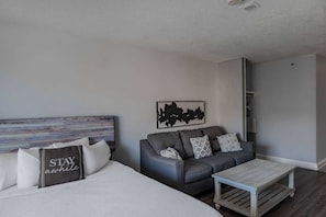 A modern bedroom with a bed, a grey sofa, a coffee table, and a wall art piece.