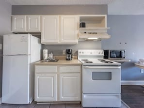 A kitchen with white cabinets, a refrigerator, a stove, a microwave, and a coffee maker.