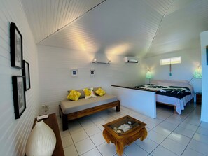 A room with a sofa, a bed, a wooden coffee table, and a wall-mounted air conditioner. - Romantic bungalow with stunning views and swimming pool (TUMARAA)