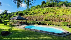 A swimming pool surrounded by lush greenery, a gazebo, and a hillside.