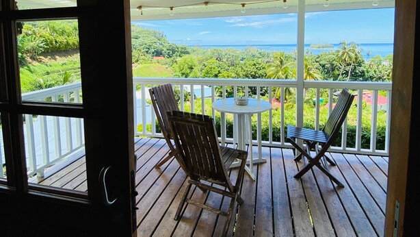 A wooden deck with two chairs and a table, overlooking a lush landscape and ocean.