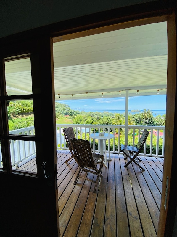 Une terrasse en bois avec deux chaises et une table, offrant une vue sur un paysage luxuriant et l’océan.