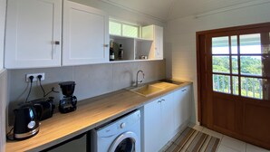 A compact kitchen with white cabinets, a wooden countertop, a washing machine, and a window with a view of greenery.