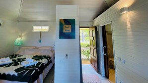 A bedroom with a bed, a wall-mounted light, a door leading outside, and a sign that says "Good Vibes".