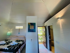 Une chambre avec un lit, une lampe fixée au mur, une porte donnant sur l’extérieur et une pancarte indiquant « Bonne ambiance ».