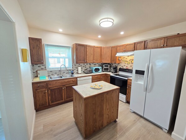 A modern kitchen with wooden cabinets, a central island, a built-in oven, and a refrigerator.
